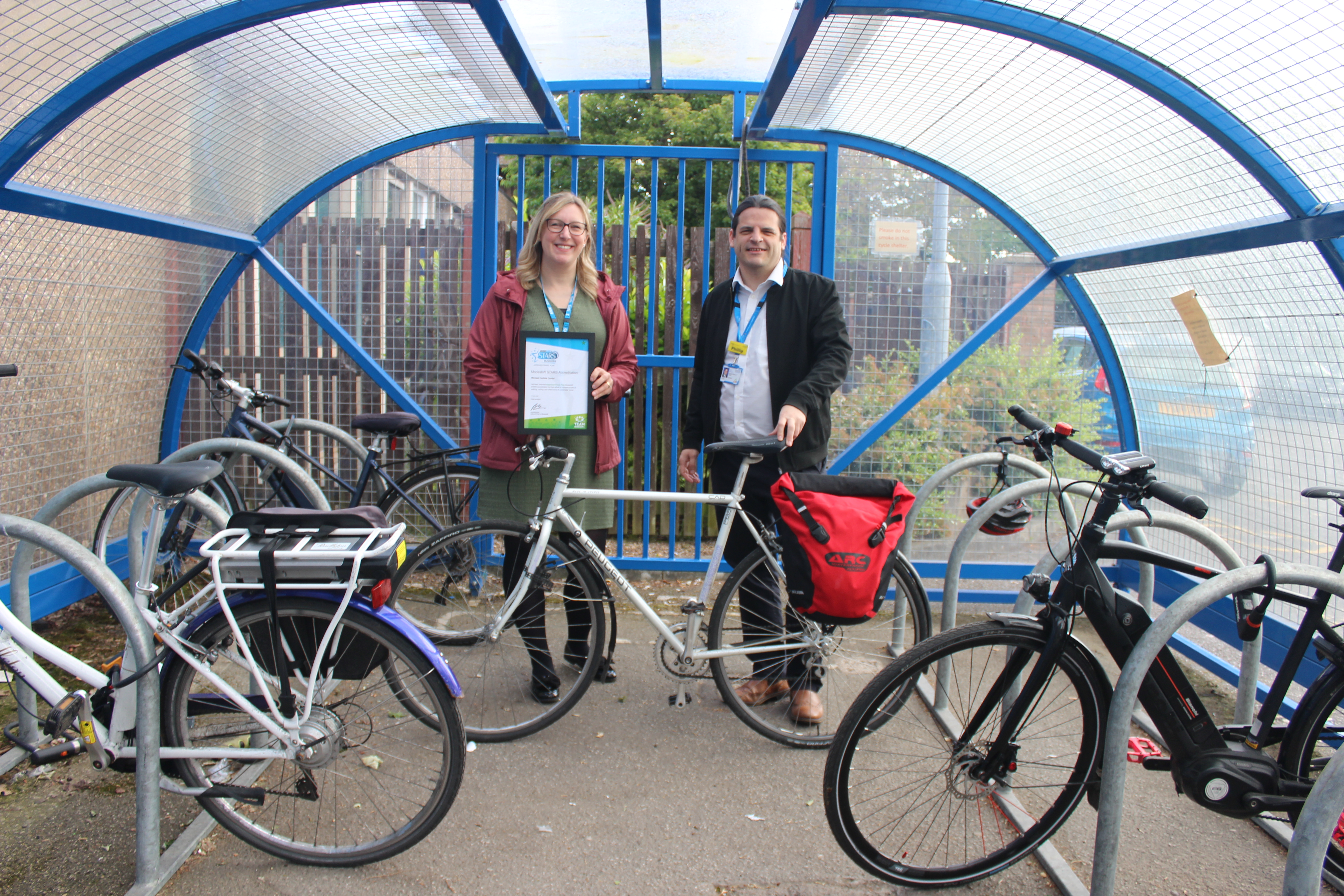 Two people stand in a bike shelter holding a certificate